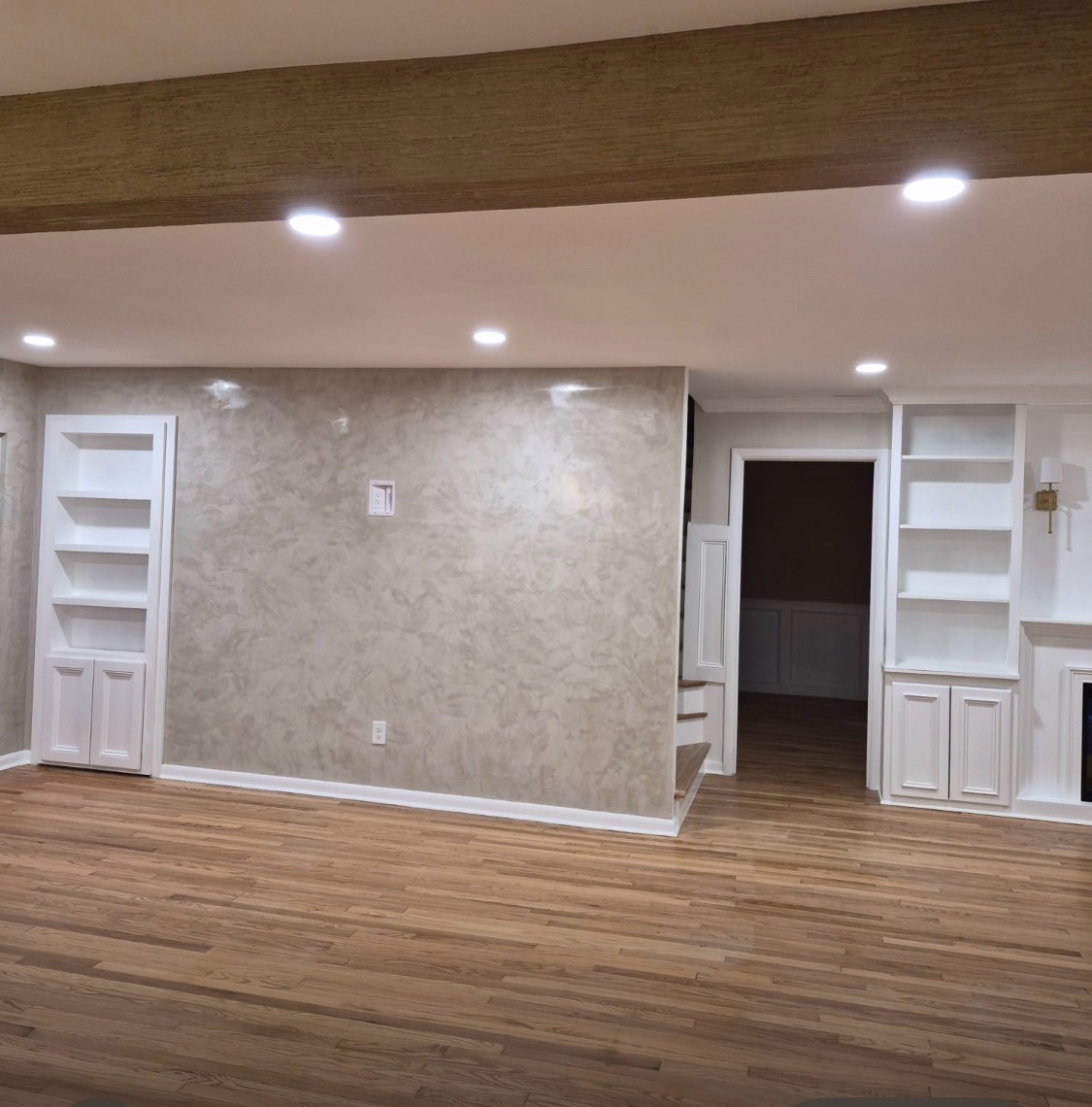 Open-plan room with a grey Venetian plaster feature wall, white built-in shelving and a wood-look ceiling beam