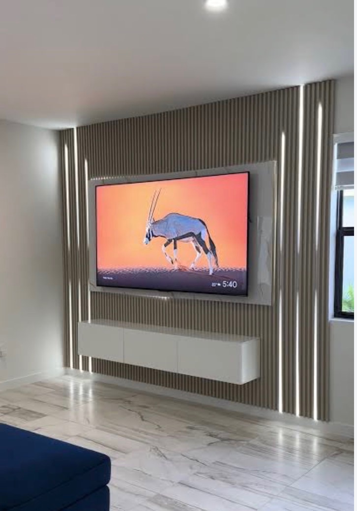 Taupe slat wall with two vertical LED reveals either side of the television and a white floating console