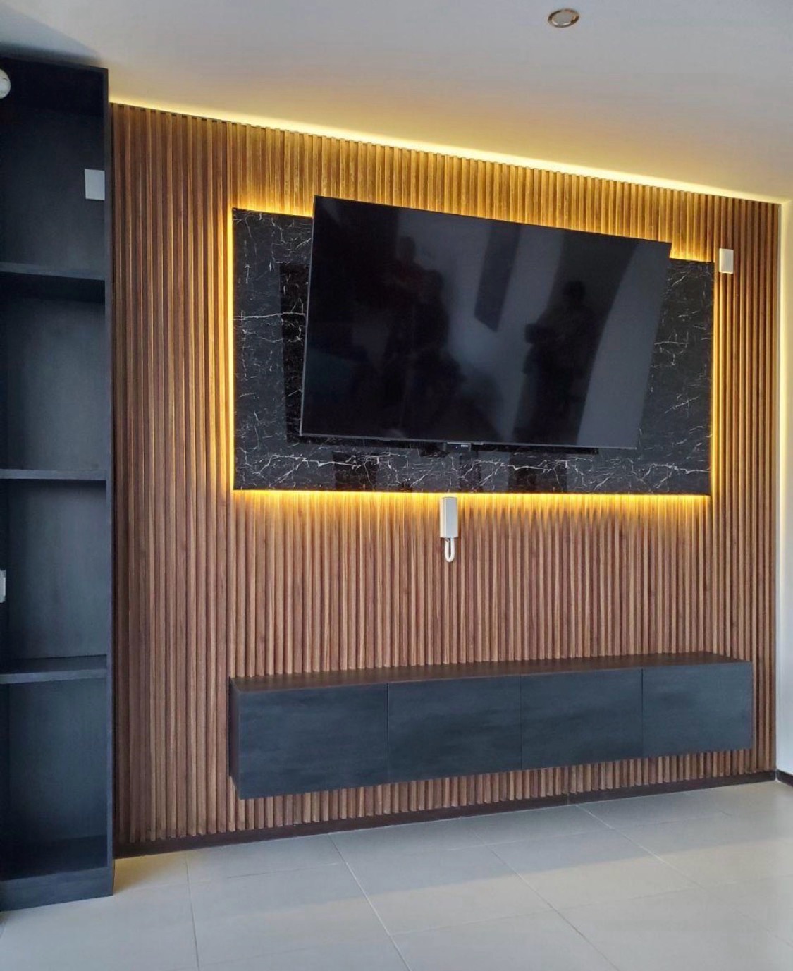 Walnut slat TV wall with a backlit black marble inlay, a floating charcoal console and open black shelving